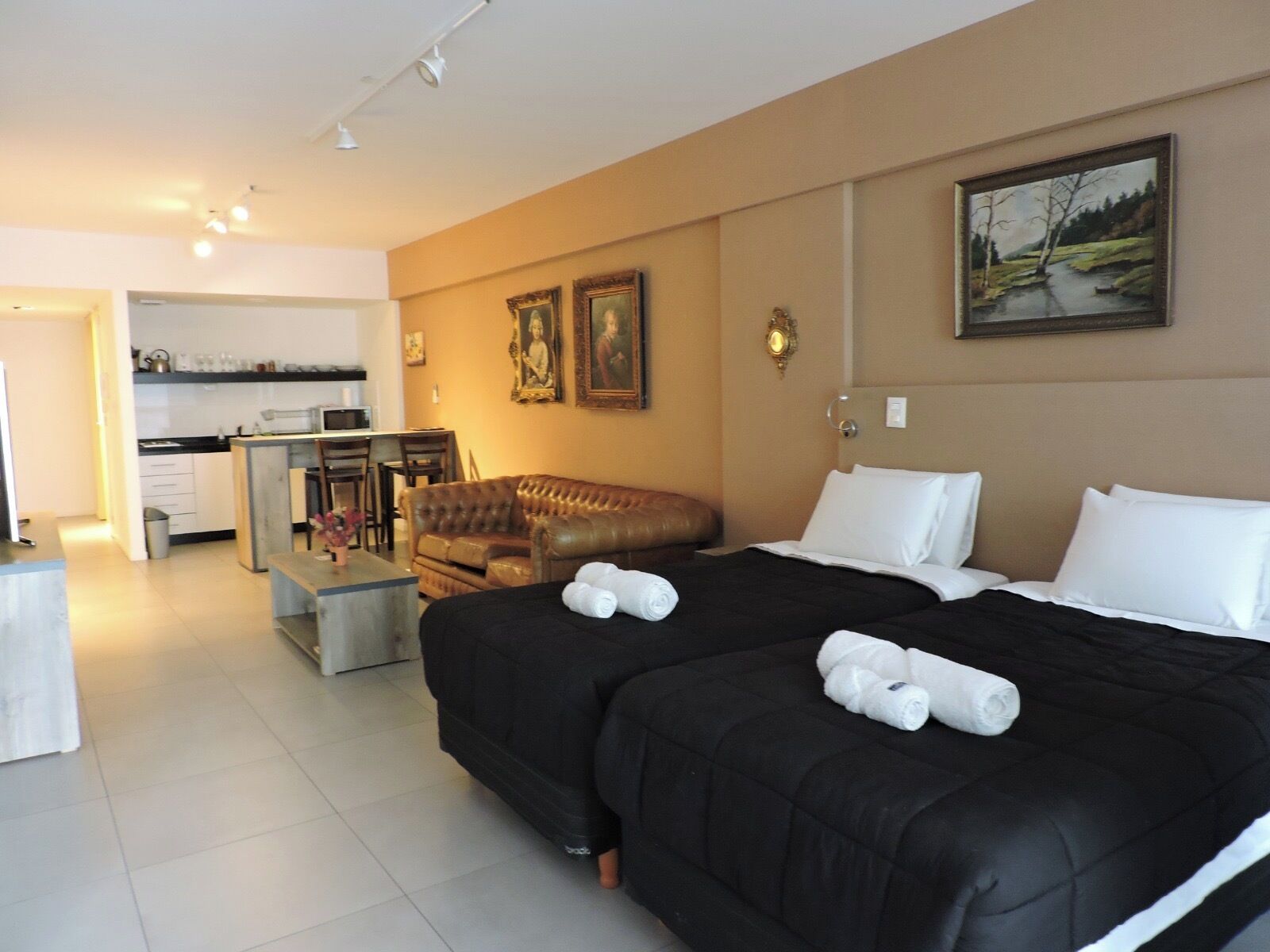 A hotel room with a large bed, a sofa, a desk, and a kitchen area.