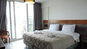 A hotel room with a large bed, a wooden headboard, a bedside table, a chair, and a view of the city through the window. - Rivadavia Apartments (Buenos Aires)