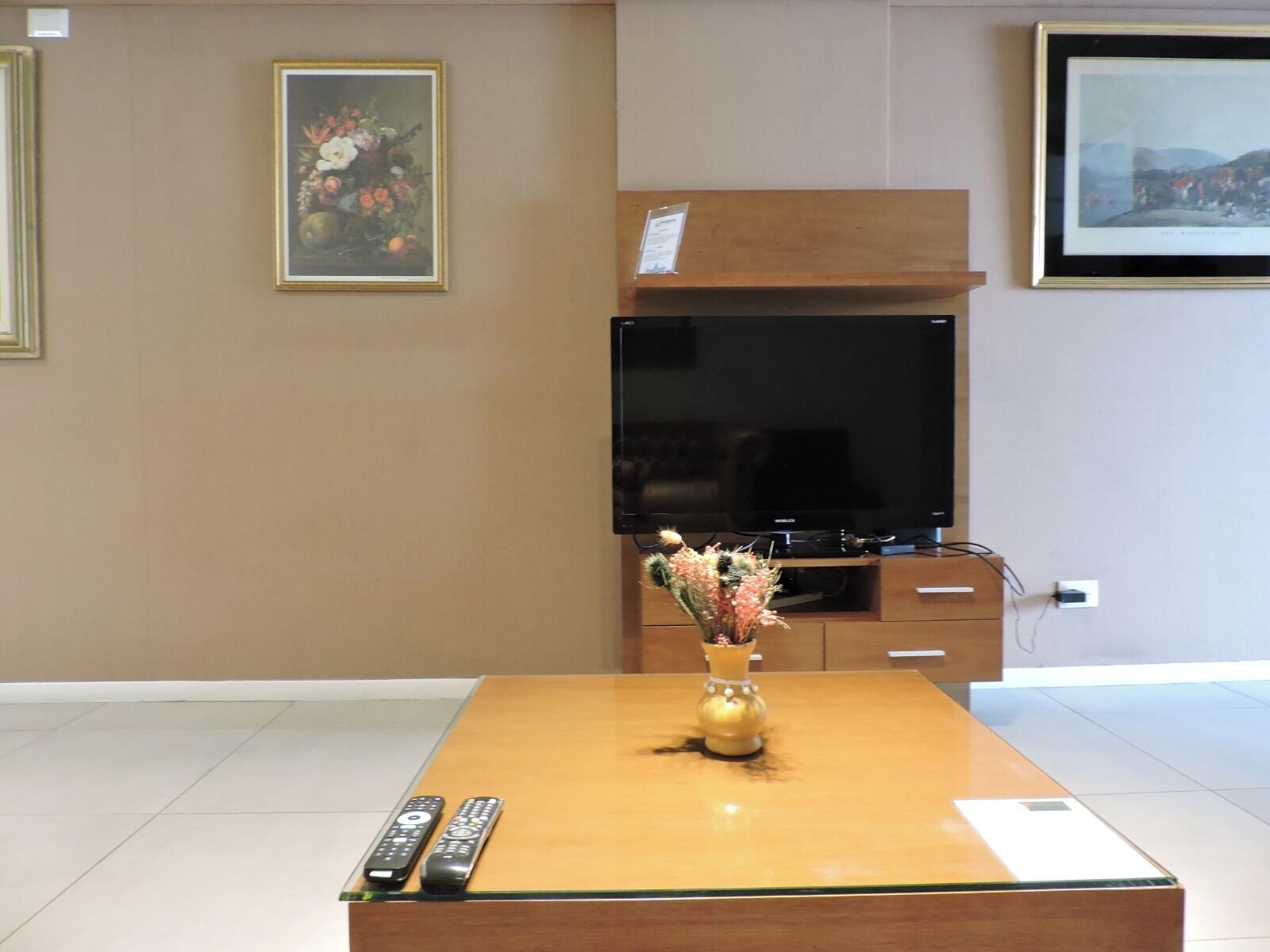 A room with a wooden coffee table, a flat-screen TV, and a vase with flowers.