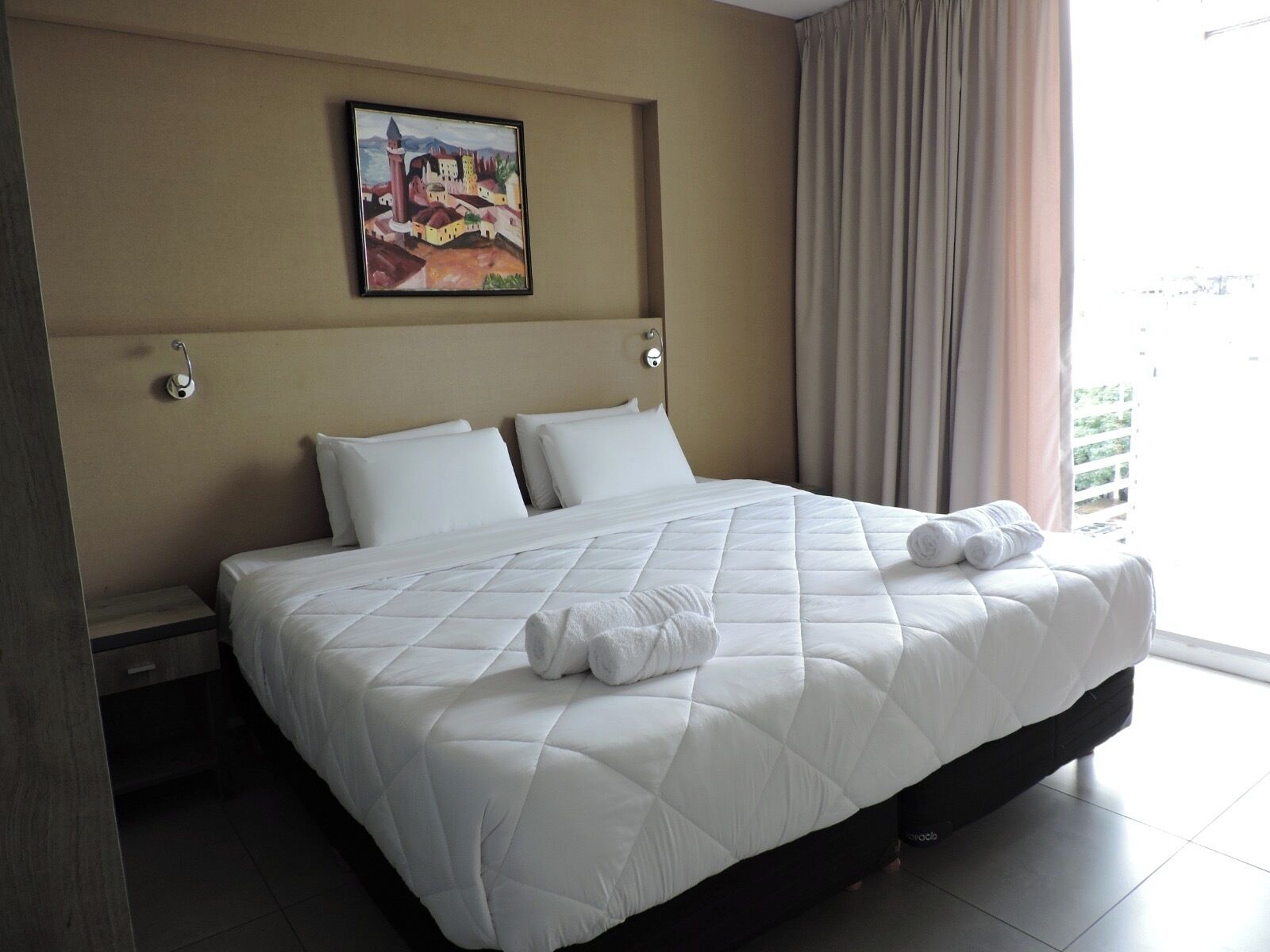 Een hotelkamer met een groot bed, een schilderij aan de muur en uitzicht op groen.