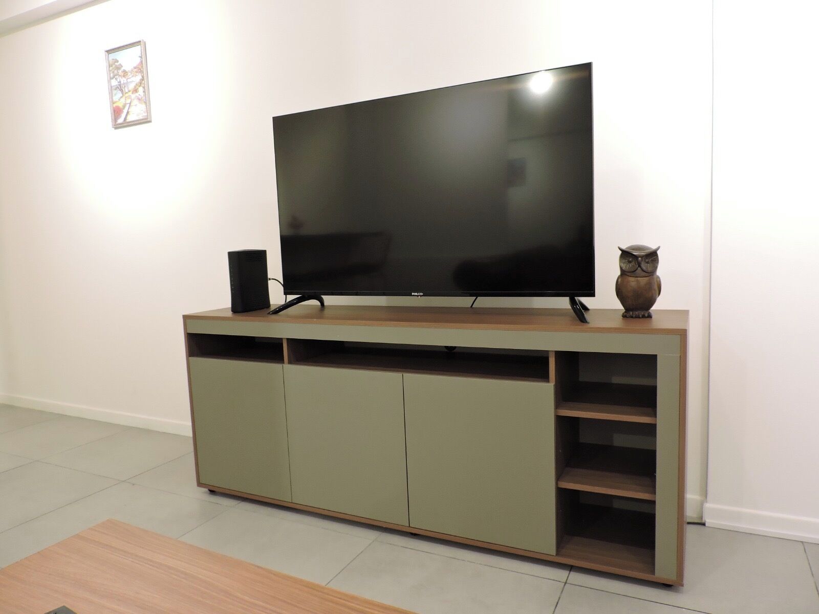 A flat-screen TV on a wooden TV stand with a shelf below and an owl decoration.