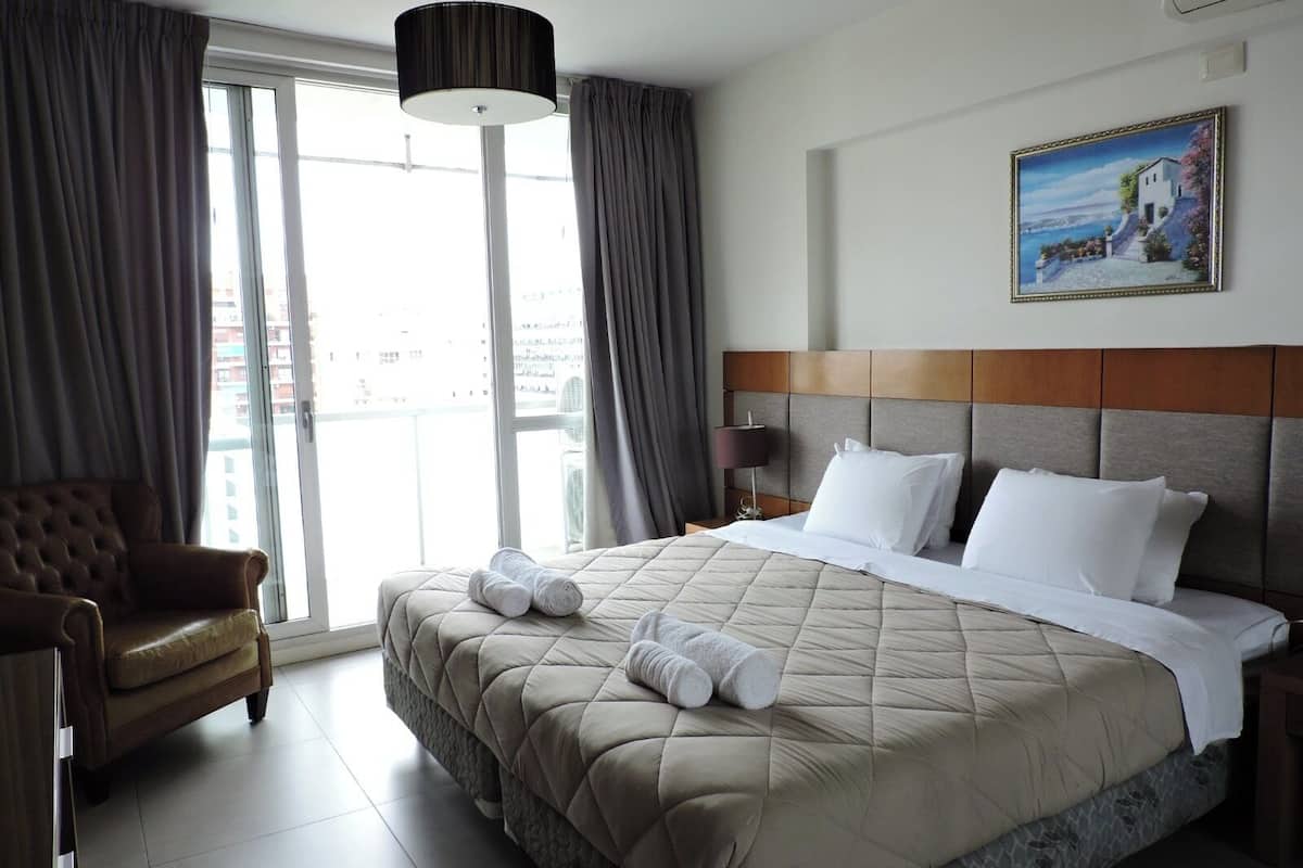 A hotel room with a large bed, a chair, a nightstand, a lamp, and a painting on the wall.