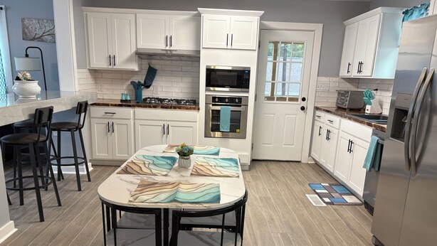A modern kitchen with white cabinets, a marble countertop, and a dining area with a round table and chairs.
