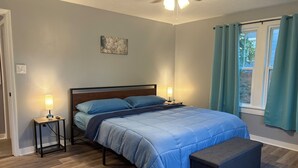 A bedroom with a bed, bedside lamps, a ceiling fan, a window with curtains, and a small table with a lamp.