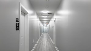 A long, narrow hallway with white walls and a wooden floor, featuring a sign for accessible rooms and an exit sign. - Tourist Homes of Richmond Church Hill North (Richmond)