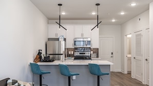 A modern kitchen with white cabinets, a central island with bar stools, and a stainless steel refrigerator. - Tourist Homes of Richmond Church Hill North (Richmond)