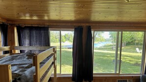A cabin with a bunk bed, a window with curtains, and a view of a grassy yard. - Tranquil cabin with AC on charming Lake Sarah.   (Erskine)
