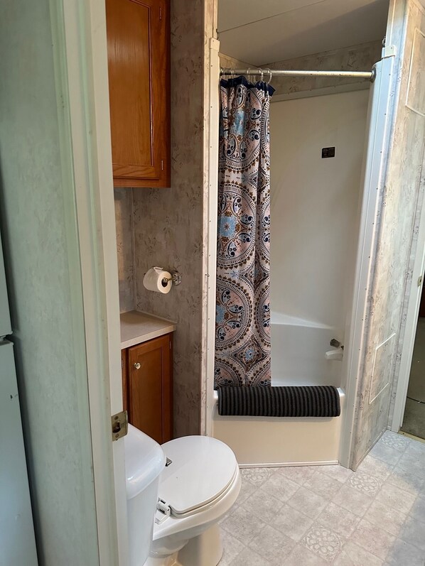 A small bathroom with a toilet, a roll of toilet paper, a shower curtain, and a bathtub.