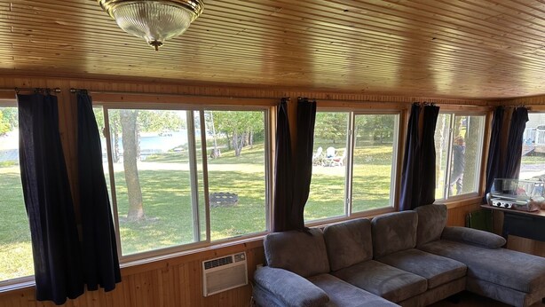 A cozy living room with a sectional sofa, large windows, and a ceiling fan. - Tranquil cabin with AC on charming Lake Sarah.   (Erskine)