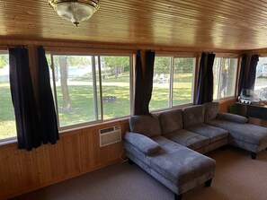 A cozy living room with a sectional sofa, large windows, and a ceiling fan.