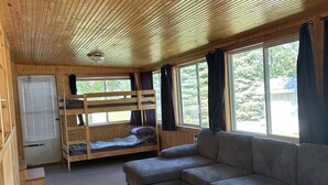 A cabin interior with a bunk bed, a sofa, and a window with curtains. - Tranquil cabin with AC on charming Lake Sarah.   (Erskine)