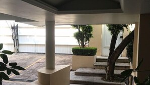A covered outdoor area with a tiled floor, a small tree, and a staircase leading to an upper level.