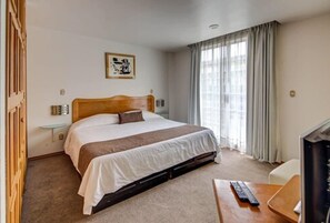 Una habitación de hotel con cama, mesita de noche, televisión y ventana con cortinas.