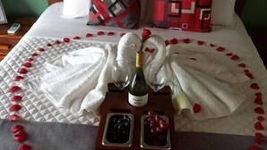 Un letto rifatto con cura, con una composizione a forma di cuore di petali di rosa, una bottiglia di champagne e due bicchieri su un vassoio.