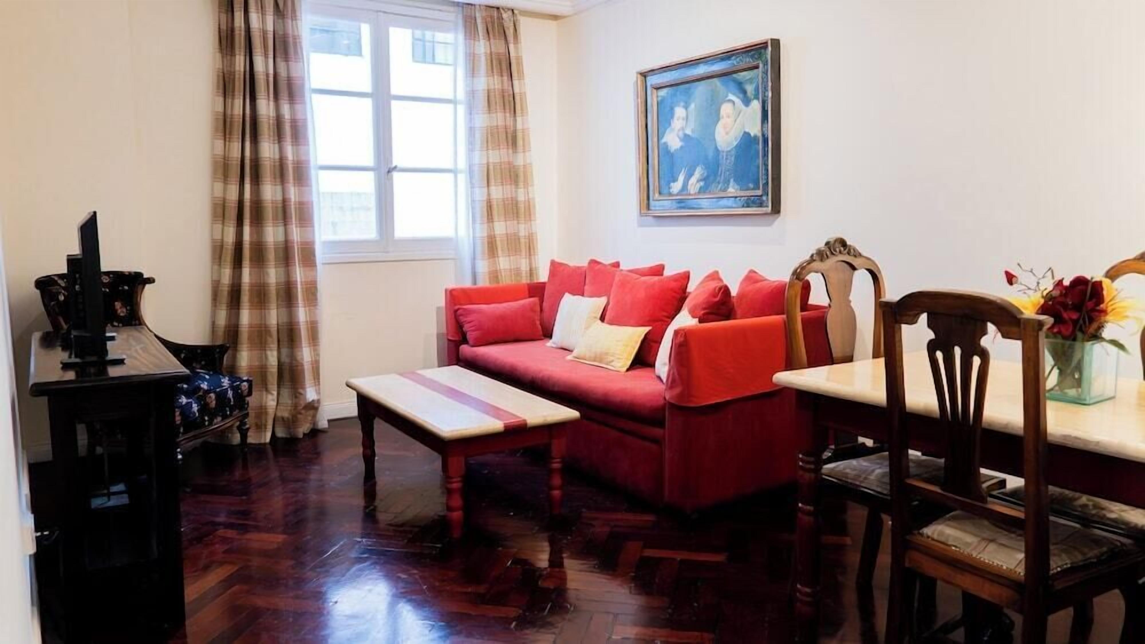 A living room with a red sofa, wooden coffee table, and a painting on the wall.