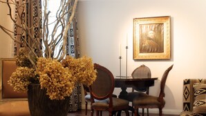Un coin repas avec une table ronde, des chaises, un vase de fleurs séchées et un tableau encadré accroché au mur.