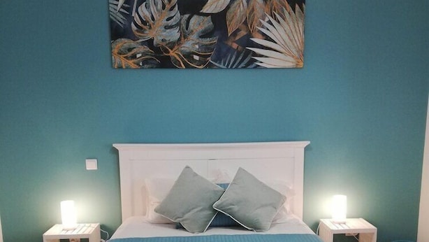 A bedroom with a white bed, teal walls, and a painting above the bed. - FX Hostel (Funchal)