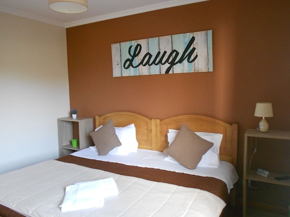 A neatly made bed with white and brown bedding, a wooden headboard, and a wall-mounted sign that reads "Laugh". - FX Hostel (Funchal)