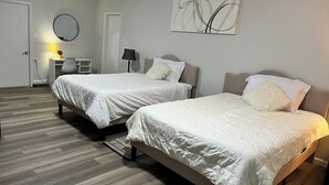 Hotellihuone, jossa on kaksi sänkyä, työpöytä, tuoli, lamppu ja seinätaideteos.