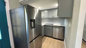 A modern kitchen with stainless steel appliances, grey cabinets, and a light wood floor.