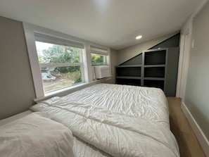 A bedroom with a large bed, a window, and a built-in shelving unit.