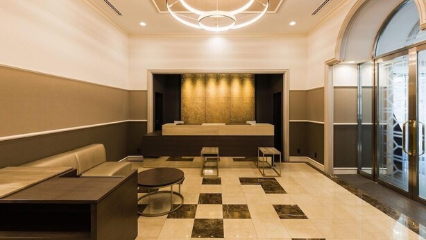 A modern lobby with a checkered floor, seating areas, a central light fixture, and a glass elevator. - Jr East Hotel Mets Musashisakai (Musashino)