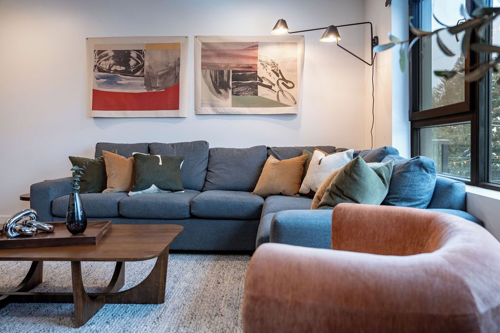 A modern living room with a grey sectional sofa, a wooden coffee table, and a large window with a view.