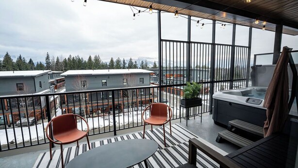 Un balcone con vasca idromassaggio, due sedie, un tavolo e vista su edifici e alberi.