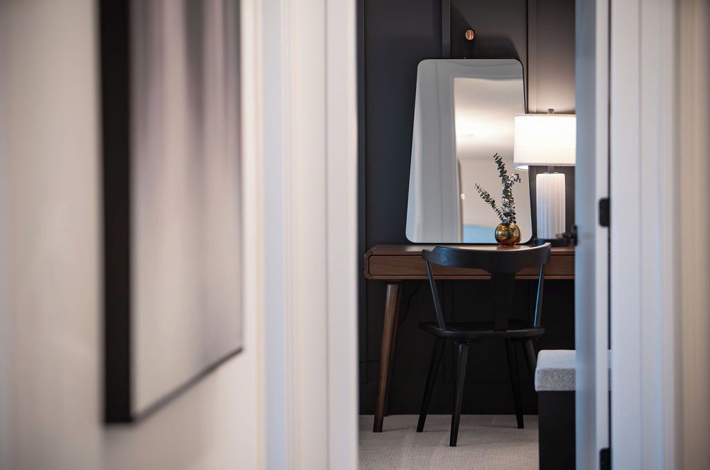A room with a wooden desk, a chair, a mirror, and a lamp.