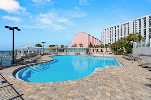 A swimming pool with lounge chairs, a building with a pink facade, and a clear sky. - Steps to the Beach - Great for Families - Beach Front Building (Miramar Beach)