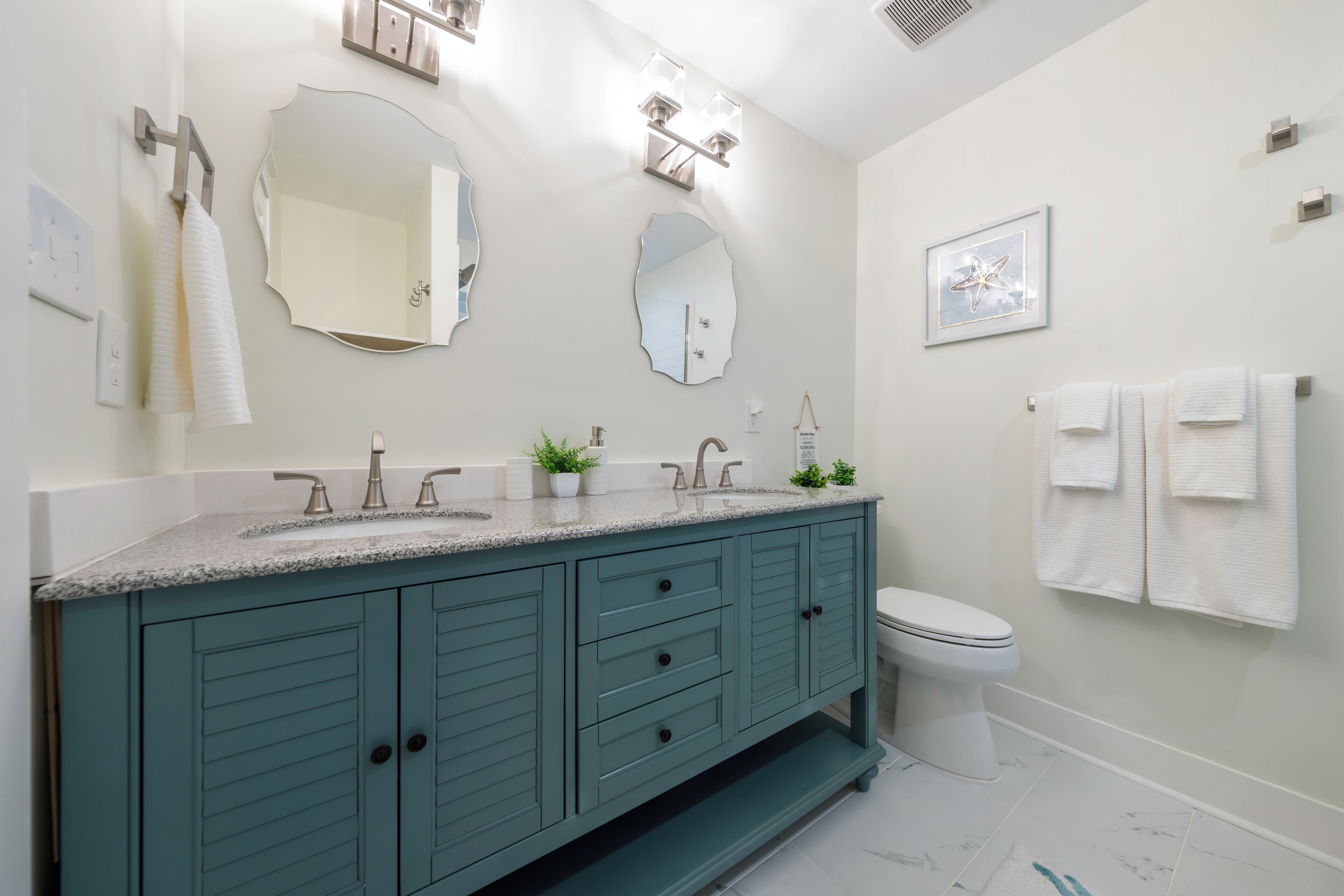 A modern bathroom with a teal vanity, a white toilet, and a large mirror.