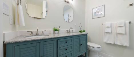 A modern bathroom with a teal vanity, a white toilet, and a large mirror.