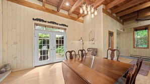 Una habitación amplia con un gran comedor de madera, varias sillas, un ventilador de techo y un ventanal con vistas a la vegetación.