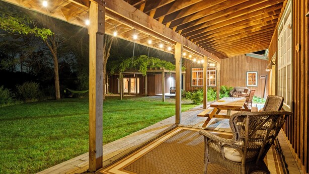 Un porche cubierto con vigas de madera, una mesa, sillas y vista al jardín trasero.