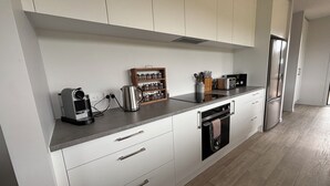Une cuisine moderne avec des armoires blanches, un four encastré et un réfrigérateur en acier inoxydable.