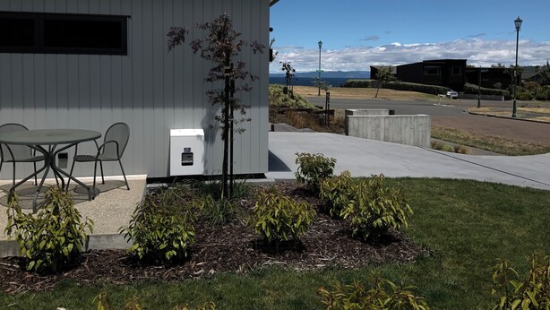A modern building with a white exterior, a small patio with a table and chairs, and a view of the ocean and mountains in the background.