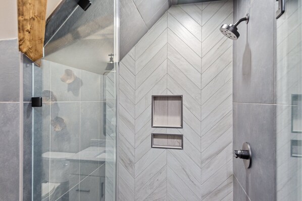 Un baño moderno con patrón de baldosas en espiga, cabina de ducha de vidrio y retrete visible.