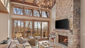 A spacious living room with a stone fireplace, a large TV mounted on the wall, and a cozy seating area with a sofa and chairs.