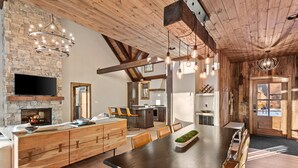 A spacious kitchen with a stone fireplace, wooden beams, and modern lighting fixtures.