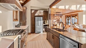 A modern kitchen with a central island, stainless steel appliances, wooden cabinetry, and a view to the dining area.