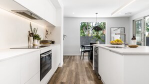 Une cuisine moderne avec des meubles blancs, un îlot central et un coin repas offrant une vue sur les arbres.