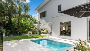 Une maison moderne dotée d’une piscine, de grandes fenêtres et d’un jardin bien entretenu.
