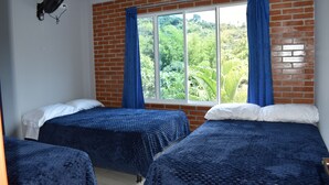 A room with two beds, a window with blue curtains, a brick wall, and a ceiling fan. - Finca el Paraiso Casa Loma, Tena (Cundinamarca)