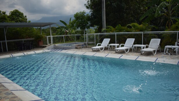 A swimming pool with clear water, surrounded by white lounge chairs and a stone-tiled edge. - Finca el Paraiso Casa Loma, Tena (Cundinamarca)