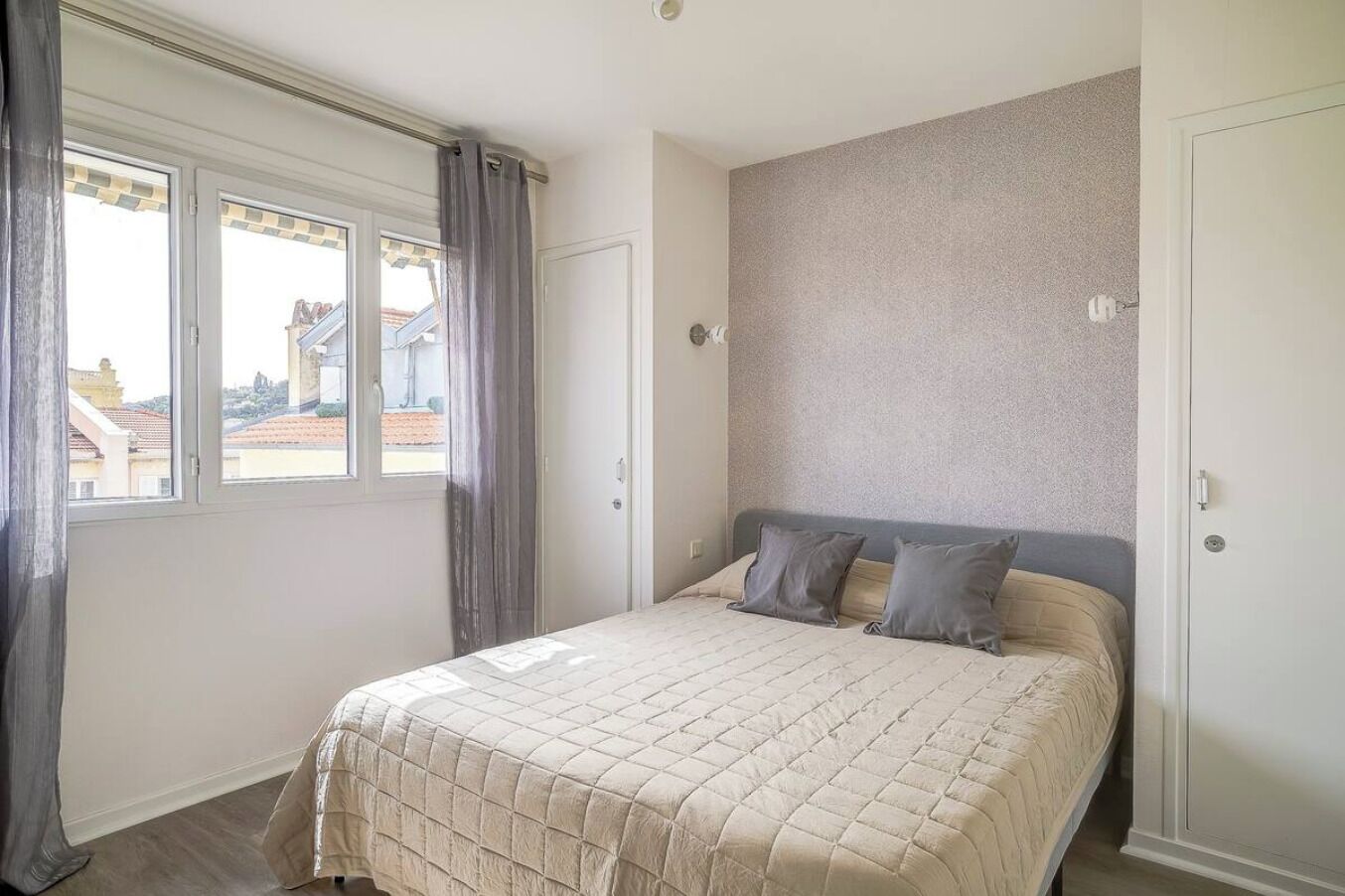 Ein Schlafzimmer mit Bett, Vorhängen und Blick auf Gebäude.