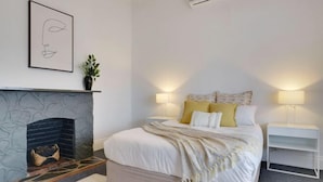 A bedroom with a bed, bedside lamps, a fireplace, and a framed artwork on the wall. - Beach & Pines Large 3Br House Glenelg Wifi BBQ (Glenelg South)