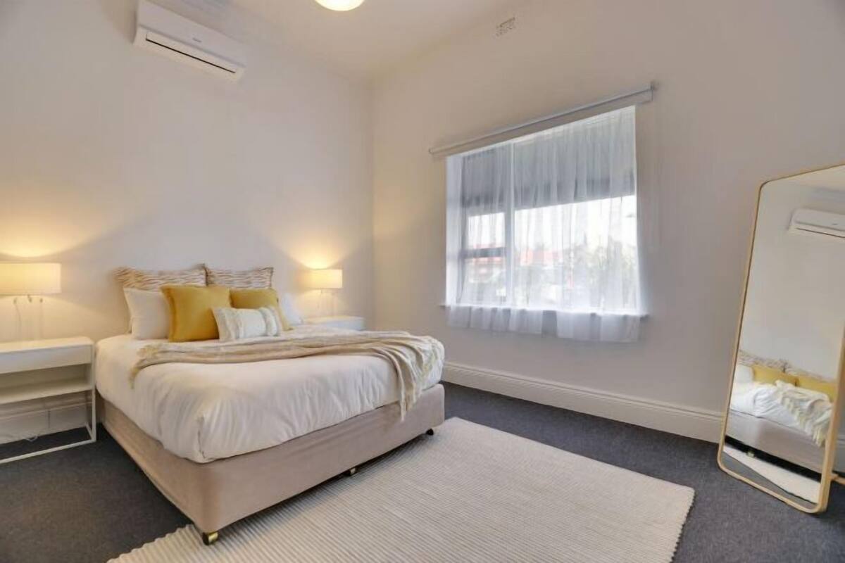 A bedroom with a bed, bedside tables, a mirror, and a window with sheer curtains.
