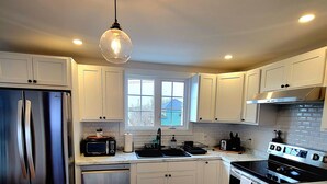 A modern kitchen with white cabinets, a stainless steel refrigerator, a black stove, and a marble countertop. - Rural Town Oasis in Bonavista  (Bonavista)