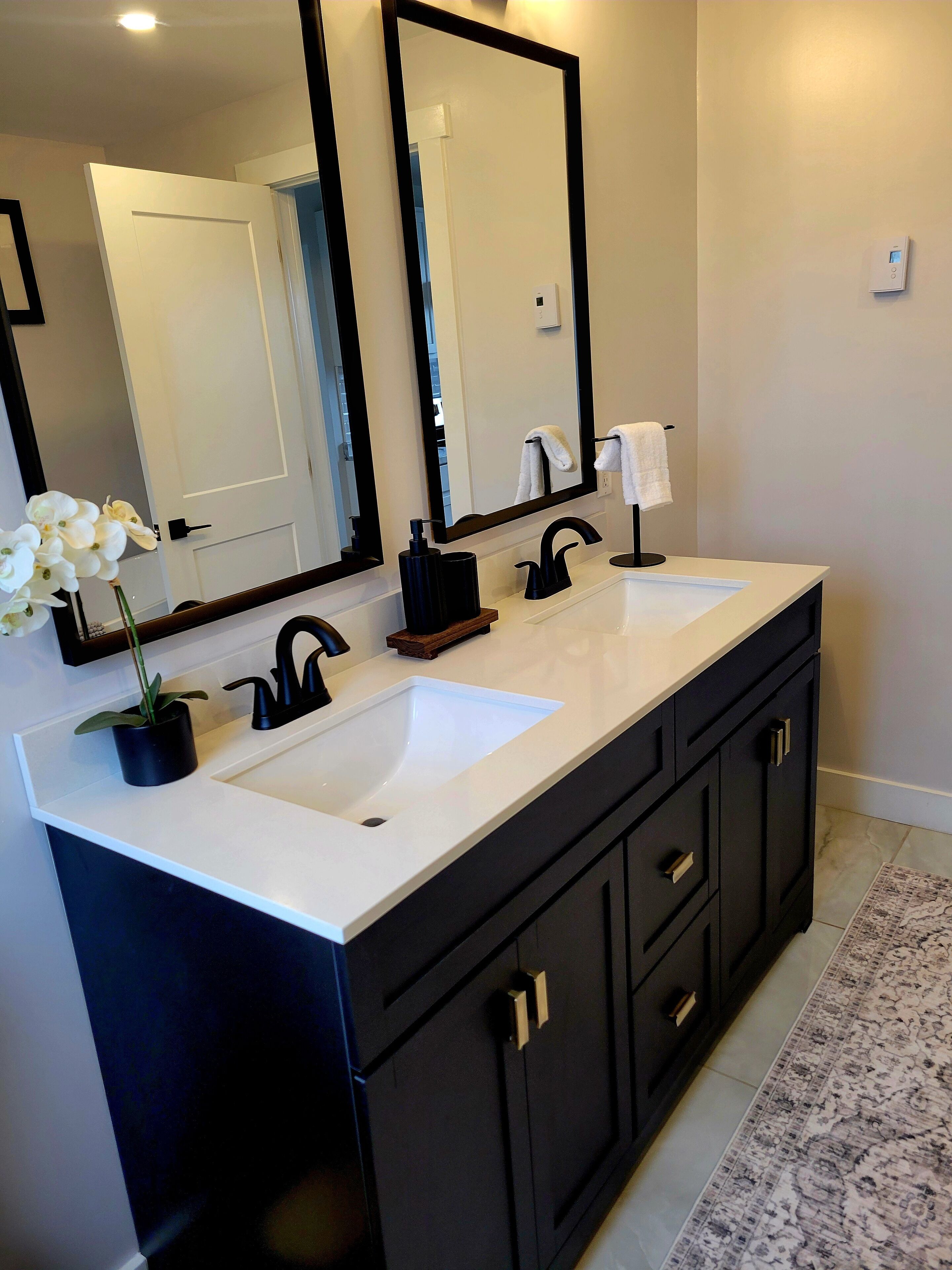 A modern bathroom with a double sink vanity, a large mirror, and a potted orchid.