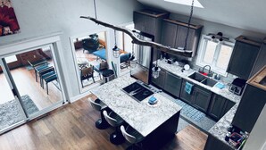 Ett modernt kök med en central köksö, mörka skåp och en matplats med utsikt över omgivningen.